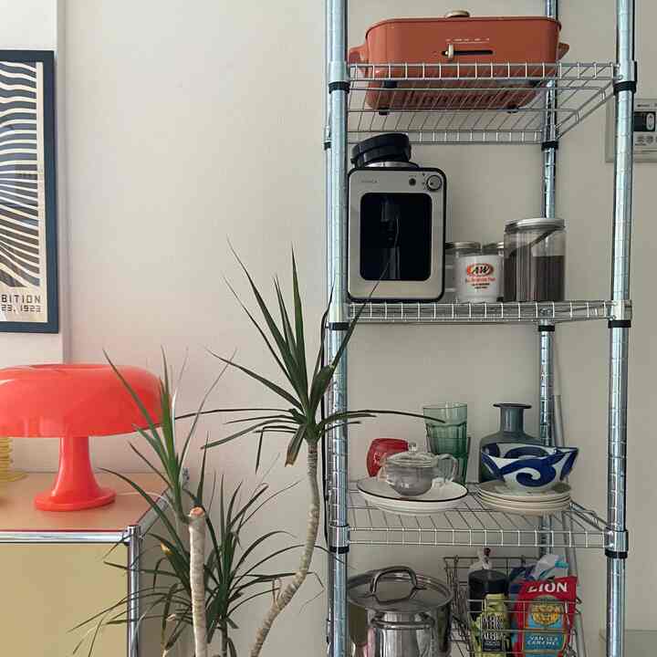 白い壁とメタルの棚、オレンジ色のテーブルランプと植物が配置されたミッドセンチュリーモダンなキッチンスペース