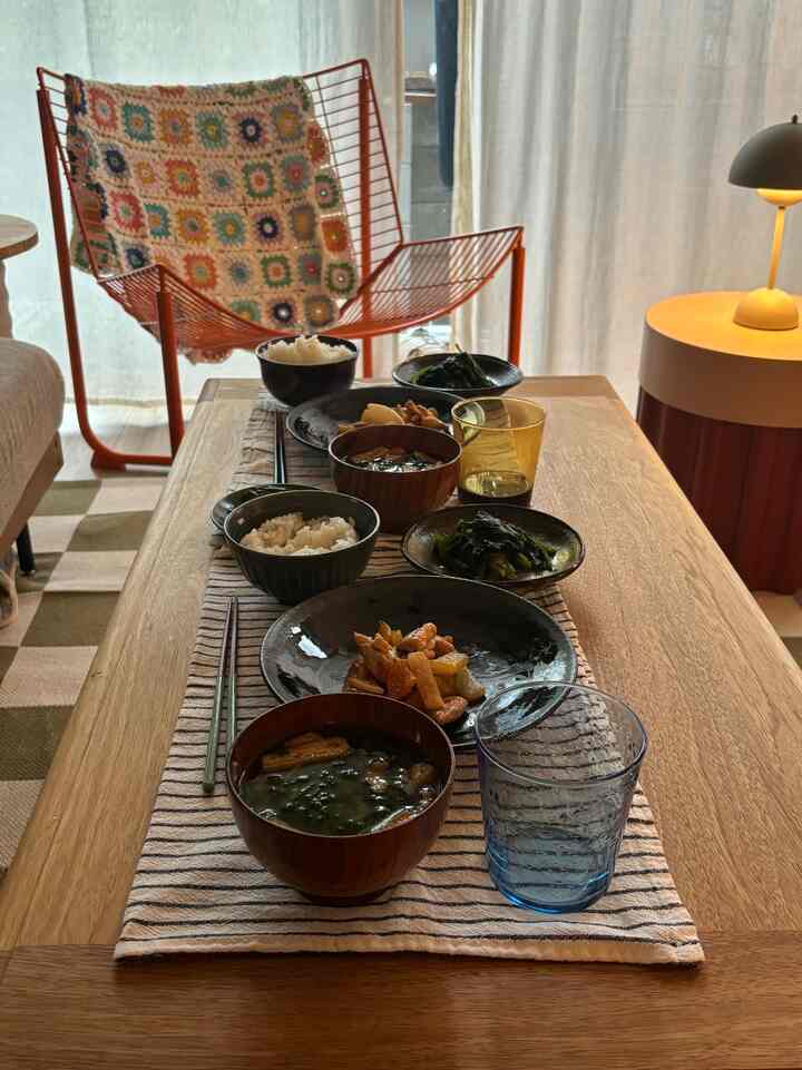 ナチュラルな色調のリビングルーム、木製のダイニングテーブルにストライプのリネンのランチョンマットと食器が配置された雰囲気のあるインテリア