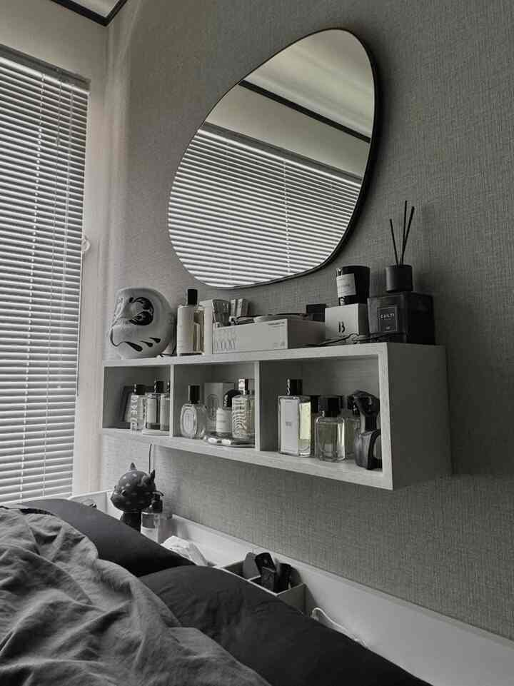 グレーの壁紙とブラインドのある寝室、白い棚に香水とキャンドルが置かれたナチュラルモダンな雰囲気の空間