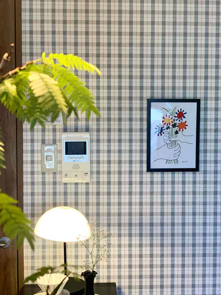 チェック柄の壁紙が背景のキッチン空間、中央右にピカソの花束ポスターが額縁に入って飾られ、左前方に植物と照明が配置された雰囲気のあるインテリア