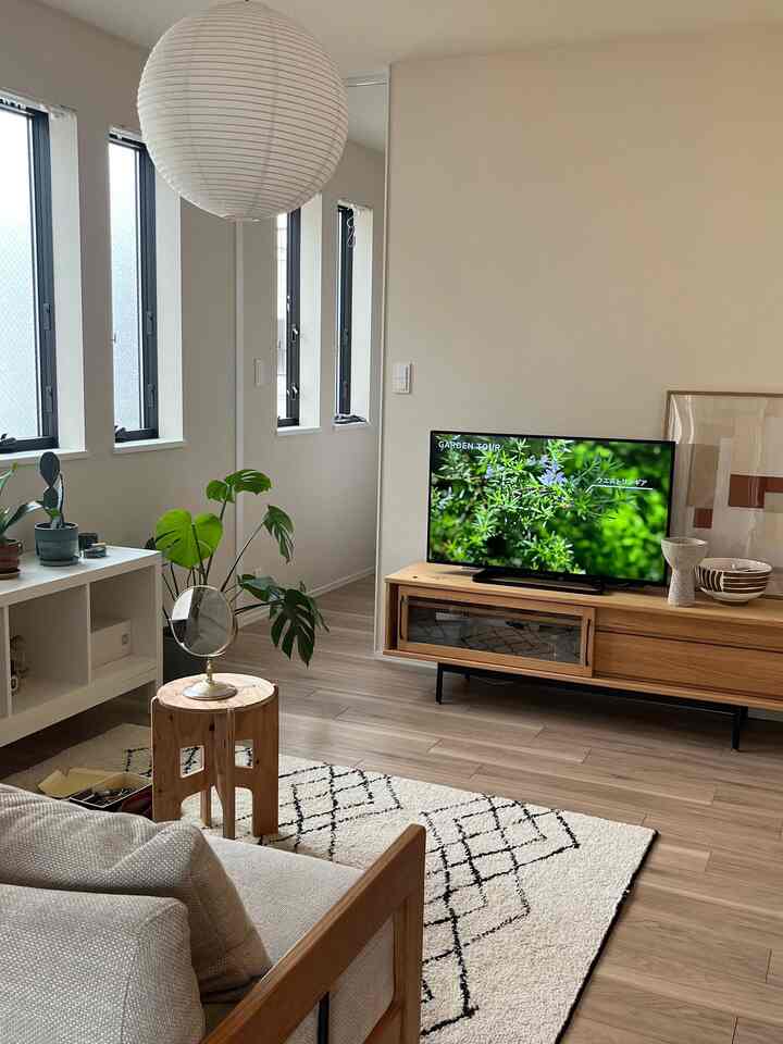 Bright ivory walls and wood-tone furniture blend in this 2LDK Nordic living room featuring a sofa and TV stand, creating a cozy atmosphere