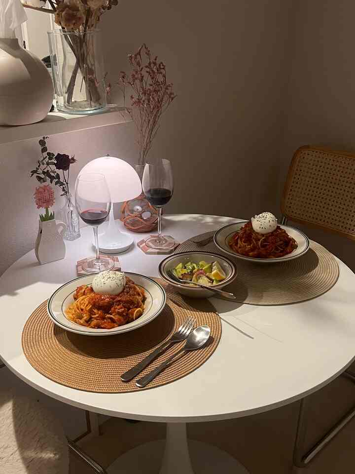 暖かみのあるベージュと白のトーンでまとめられた、小さな丸いダイニングテーブルにパスタとワイングラスが並ぶ印象的な2人用空間