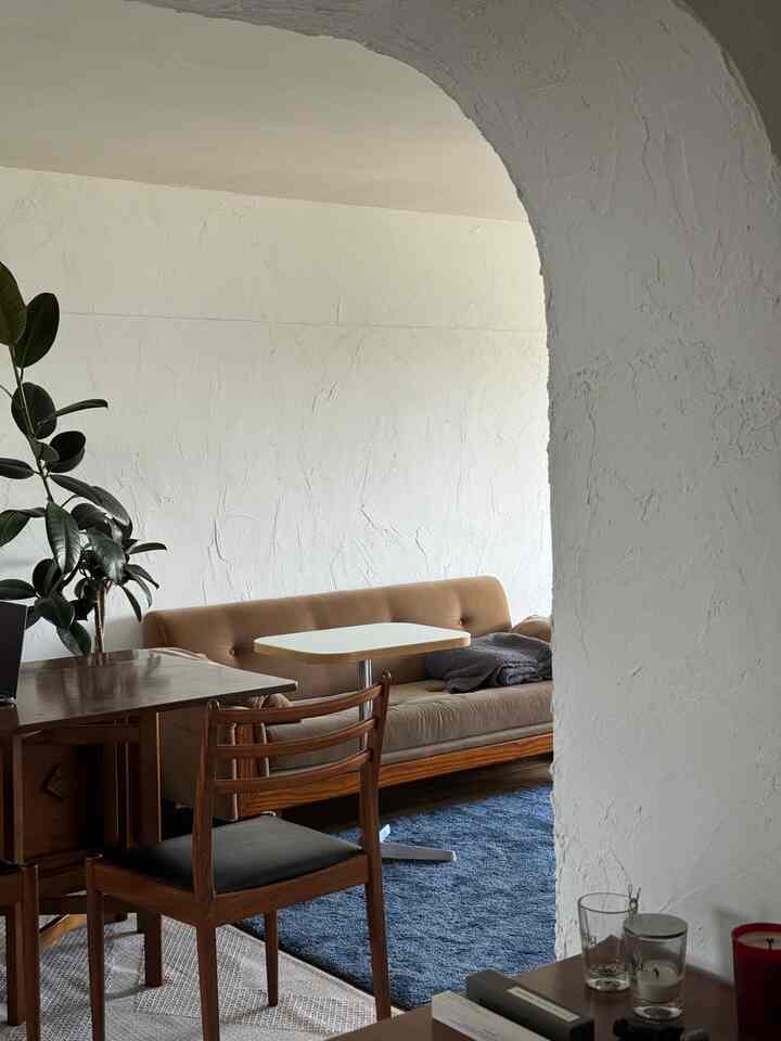 白い質感の壁と木目調家具が調和したミッドセンチュリーモダンのリビング、青いラグとダイニングチェアが配置された落ち着いた空間