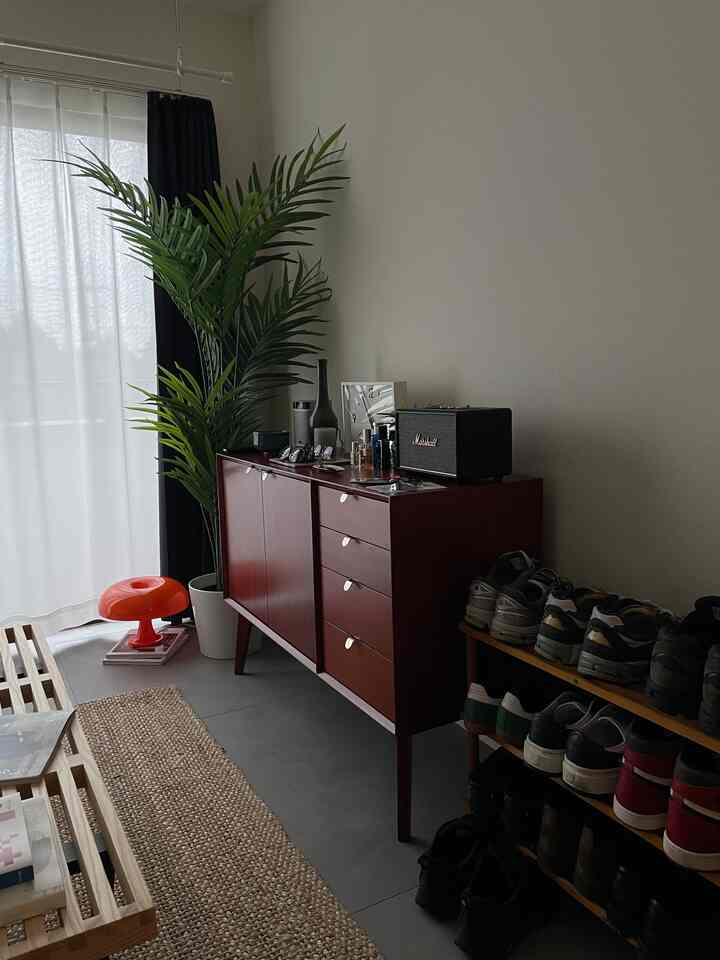 白い壁と木目調の家具が配置された北欧風のシンプルなリビング、印象的な大きな観葉植物とスピーカーが目を引く空間