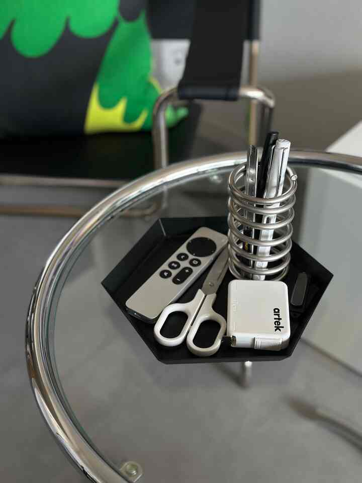 黒いトレイと銀色の文房具が置かれたガラスのサイドテーブルと黒いオフィスチェアが配置されたモダンな空間