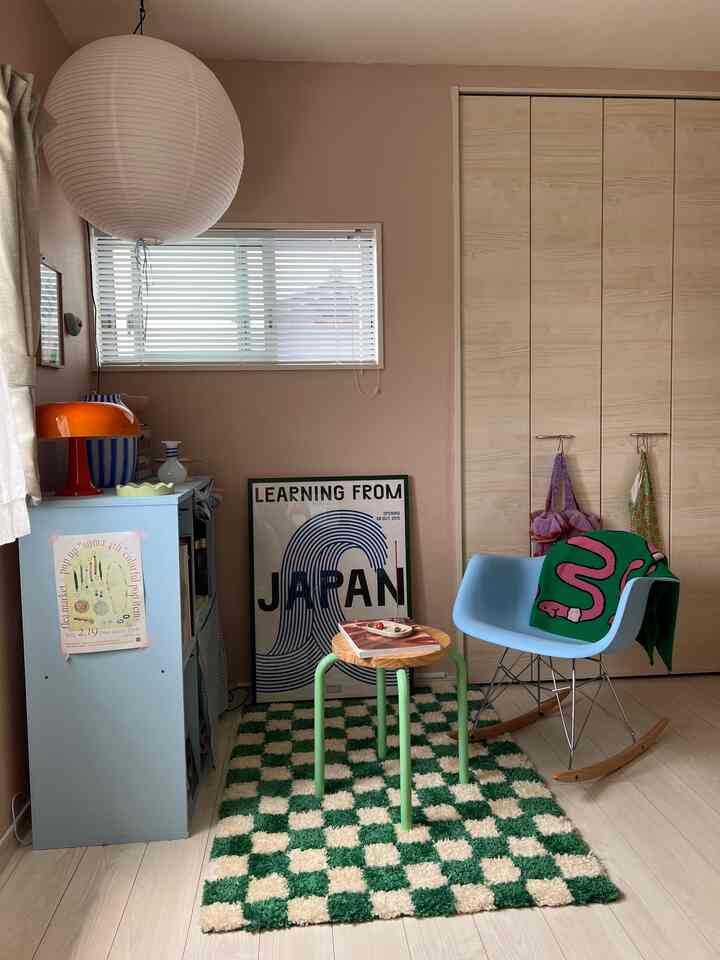 ピンクの壁とスカイブルーの家具が配置された居心地の良いホームオフィス、チェッカー柄のラグとロッキングチェアが配されている