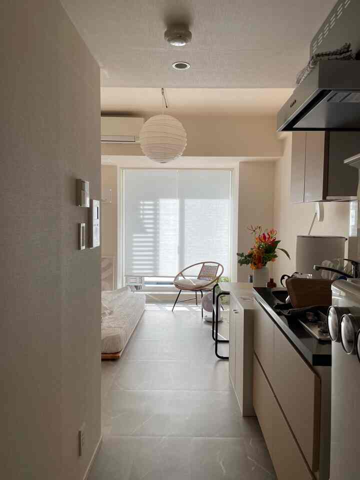 White and beige toned studio apartment kitchen-living area featuring a simple bed frame and blinds with minimalistic interior