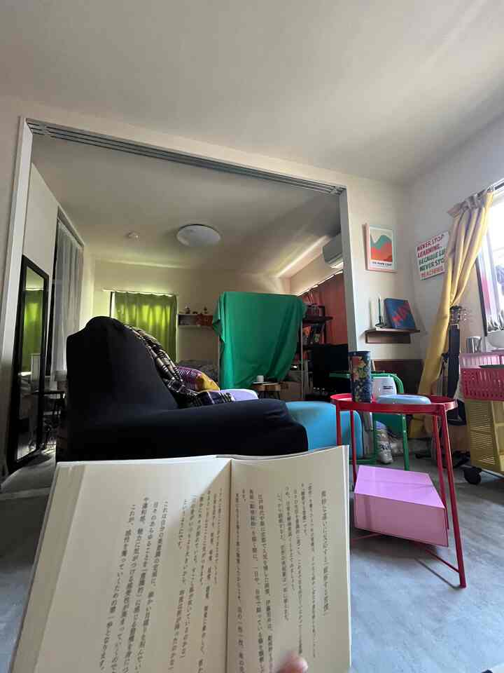Bright yellow curtains and colorful cluttered living area partitioned by green fabric, featuring black sofa and side tables