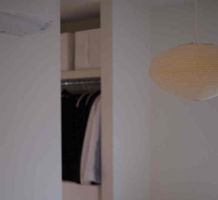 柔らかな自然光が差し込む白い寝室、イサム・ノグチのペンダントライトと整頓されたウォークインクローゼットが配置されたシンプルな空間