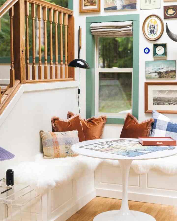 White and natural brown toned living room corner storage area featuring cozy cushions and wall sconce lighting for a warm atmosphere