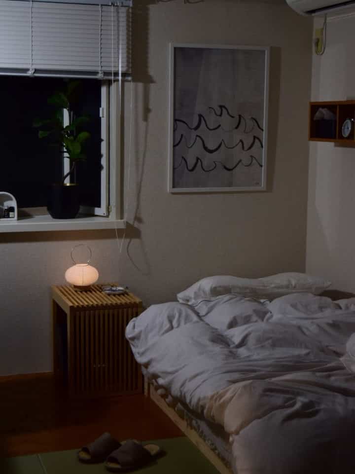 落ち着いたトーンの寝室、木目調の家具と白い寝具が配置された雰囲気のあるインテリア