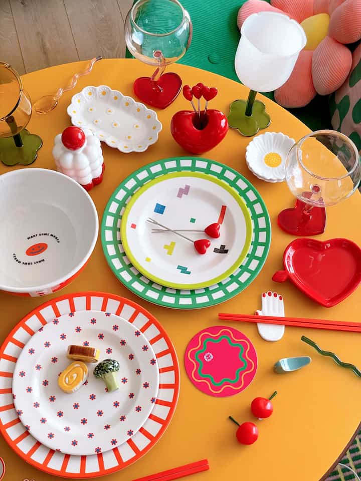 Colorful table setting on orange table featuring retro-style white plates, bowls, and red heart-shaped decor elements