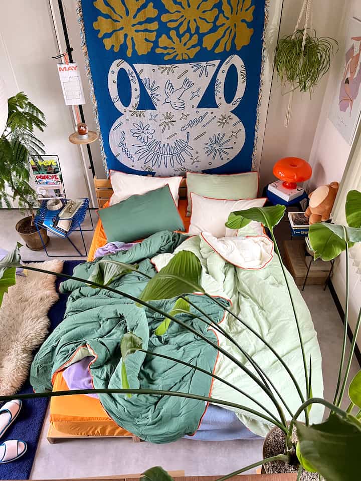 Bedroom in green and orange tones featuring colorful bedding and abundant indoor plants creating a cozy atmosphere