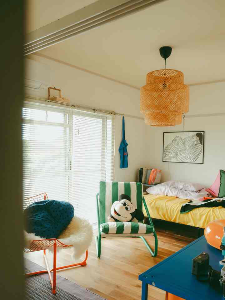 ナチュラルな木目調の床とラタンのペンダントライトがある二人暮らしのリビング、ストライプのアームチェアと鮮やかな色の椅子が配置された、雰囲気のある空間