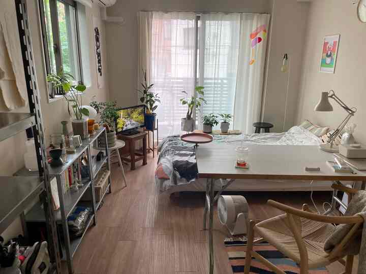 ナチュラルな木目調と白を基調とした一人暮らしの寝室、窓への動線を確保した清潔感あるレイアウト、植物とモダン家具を配置した空間