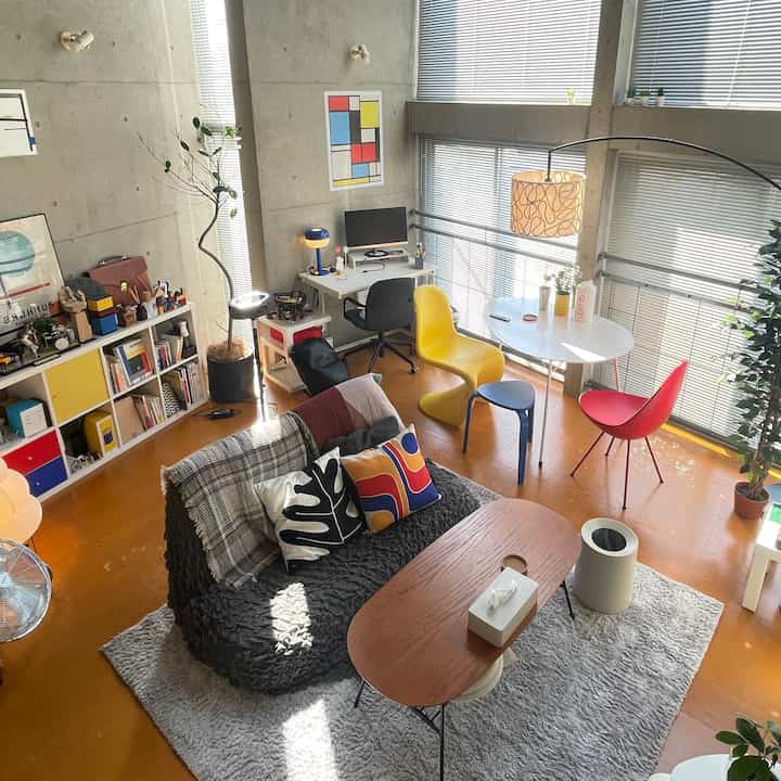 Natural-toned living room featuring colorful dining chairs, sofa, and a modern workspace with abundant natural light