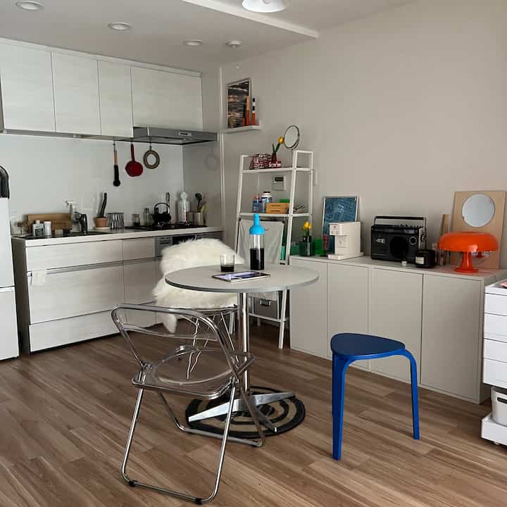 白とナチュラルウッド調のキッチン、丸テーブルとスツール、IKEAのEKET収納が配置されたミニマルなインテリア