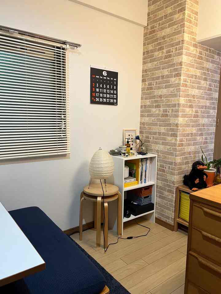 ナチュラルな木目調と白いレンガ壁が印象的な一人暮らしのリビング、イサム・ノグチのアカリフロアランプとネイビーブルーのソファが配置された清潔感あるインテリア