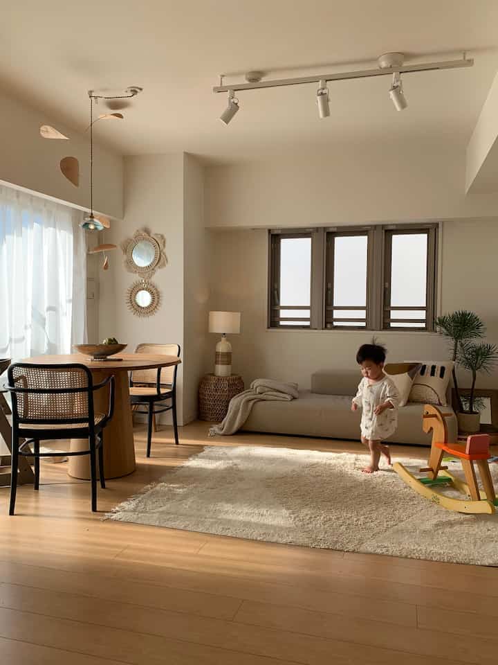A beige and white toned living and dining room featuring wood furniture, rug, and a child's play area in natural modern style
