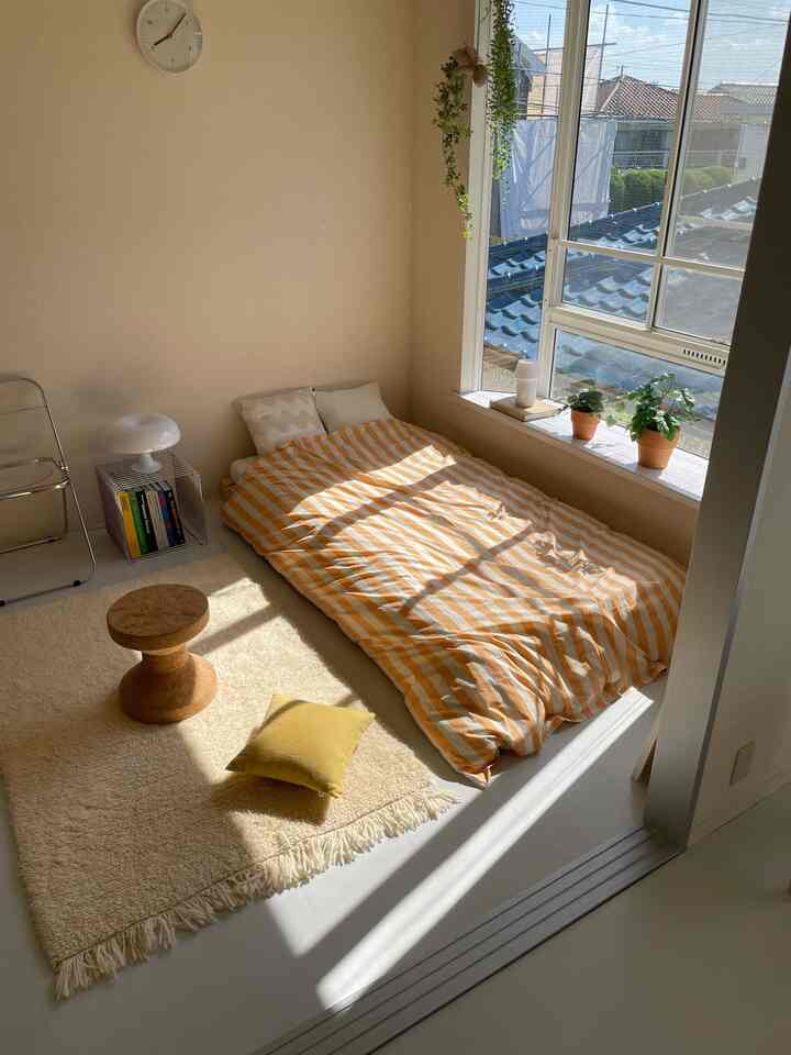 ベージュの壁とオレンジのストライプ掛け布団カバーがある寝室、日差しが差し込む自然な雰囲気のあるインテリア