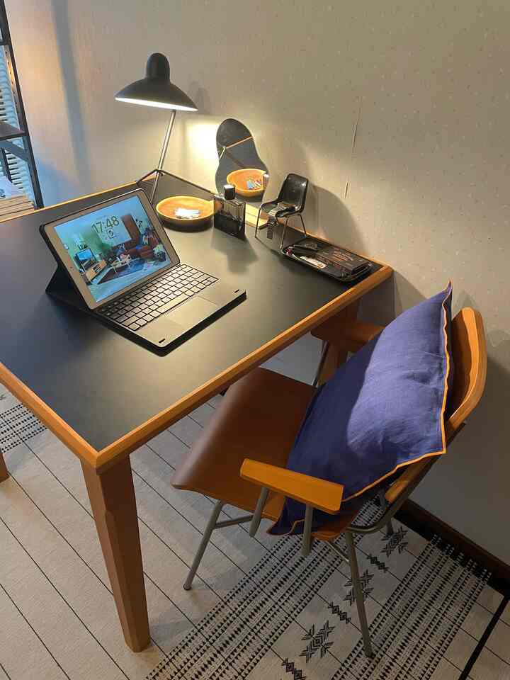 ウッドトーンと黒色が調和したミッドセンチュリーモダンのホームオフィス空間、ダイニングテーブルとデスクライト、クッションが配置された雰囲気ある作業スペース