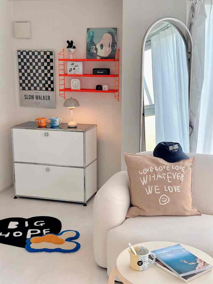 白とベージュのトーンのリビング、サイドボードと大きなスタジオミラー、ベージュのクッションが置かれたシンプルな空間