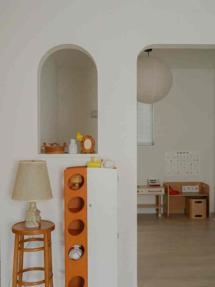 ナチュラルな色調の子供部屋、アーチ型の壁の下に木製家具とおもちゃ収納が配置された温かみのある空間