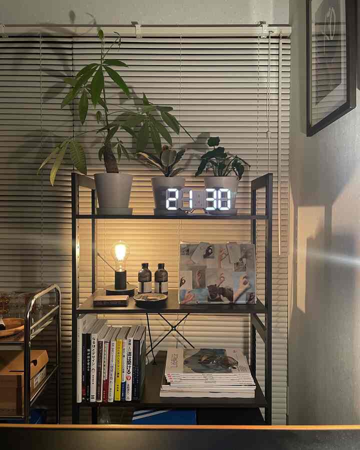 黒い金属製の棚に白いデジタル時計と観葉植物が配置されたモダンなホームオフィス空間