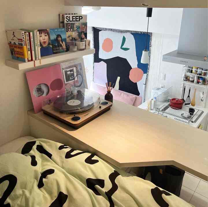 ミント色とブラックのパターンの掛け布団があるワンルームの寝室、アナログレコードプレーヤーと抽象的なウォールアートが配置された落ち着いた空間