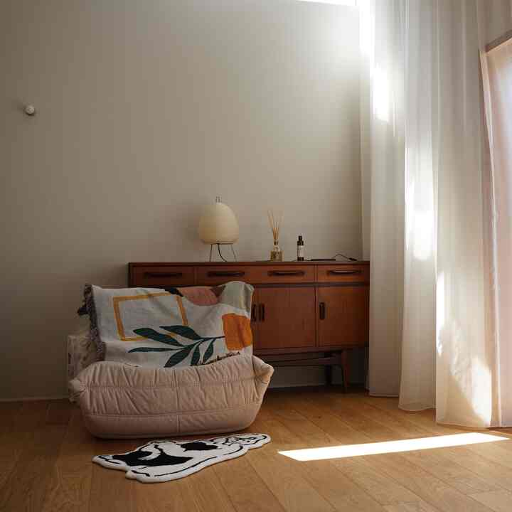 ナチュラルなベージュ色の壁と茶色の木製サイドボードが配置されたリビングの一角、居心地の良いアームチェアとフロアランプがある温かみのあるインテリア