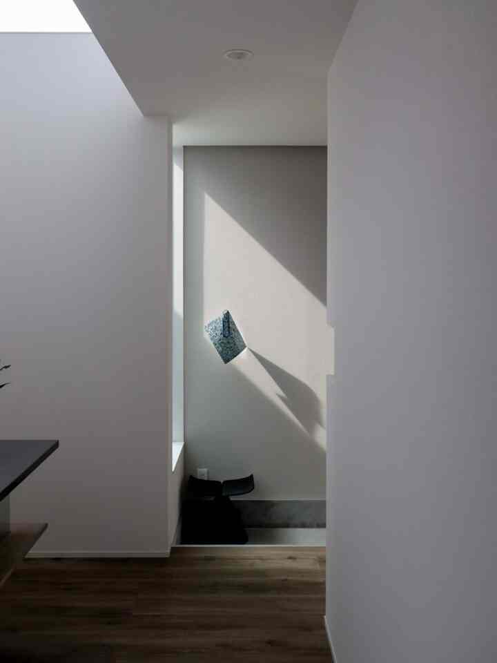 Natural narrow entrance with white walls and wood-tone floor, featuring a black stool against the wall in a minimalist setting