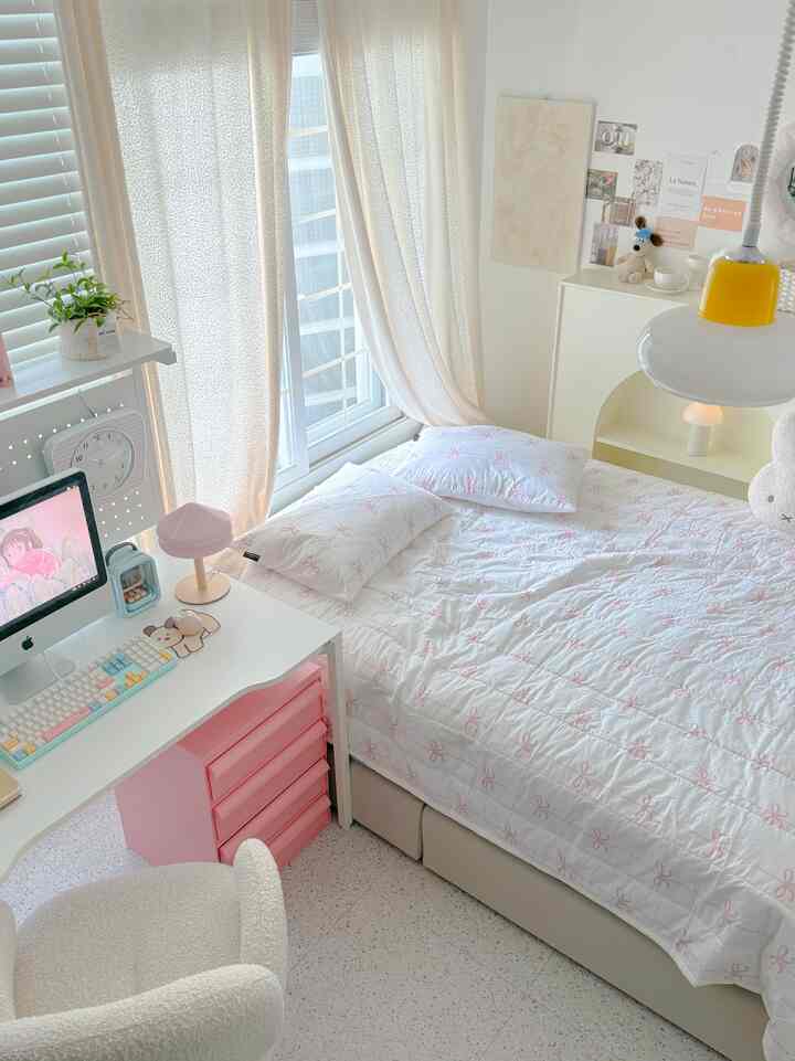 ホワイトとピンクの色調の寝室、ピンクのリボン柄の寝具とデスクが配置された清潔感のある子供部屋のインテリア