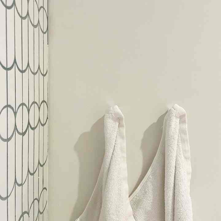 白い浴室の壁、左側には灰色の円形模様のタイルがあり、白いタオルが2枚掛けられている