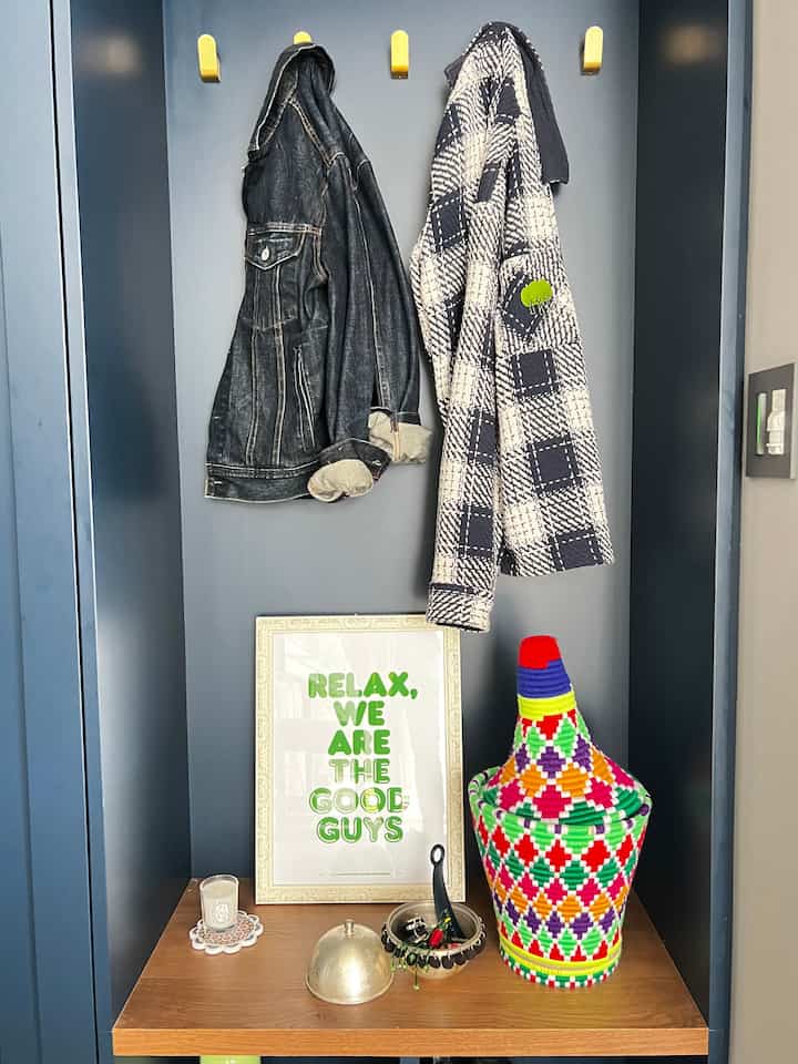 青い壁と木製ベンチが配置された玄関スペース、コート掛けにコートが掛かり、カラフルな装飾品が並ぶ印象的な空間