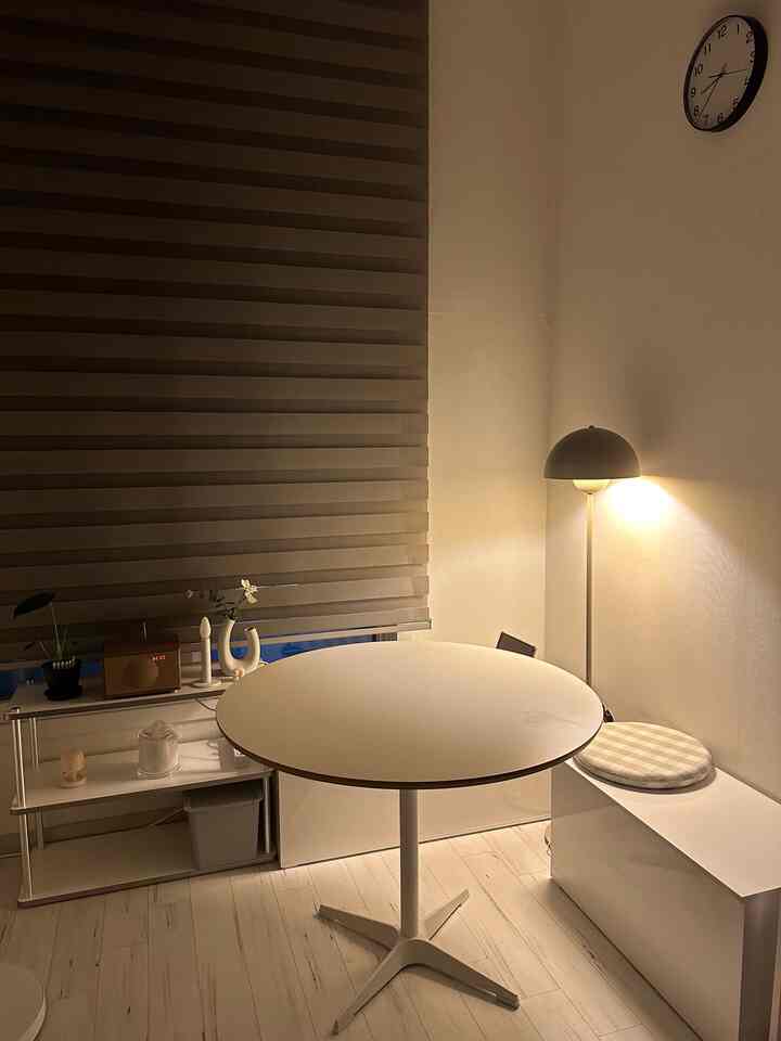 暖かい照明の小さな部屋、白い円形テーブルとシンプルな棚が配置されたミニマルな空間