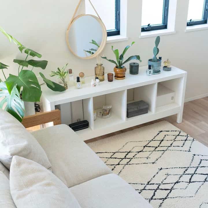 ナチュラルな色調のリビング、白いIKEAの棚とベージュのラグが配置された落ち着きのある清潔な空間