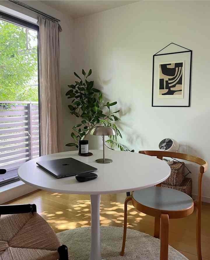 白と茶色のトーンの10畳のラウンドテーブル空間、フィカスの観葉植物とテーブルランプが配置された雰囲気のあるホームオフィスインテリア