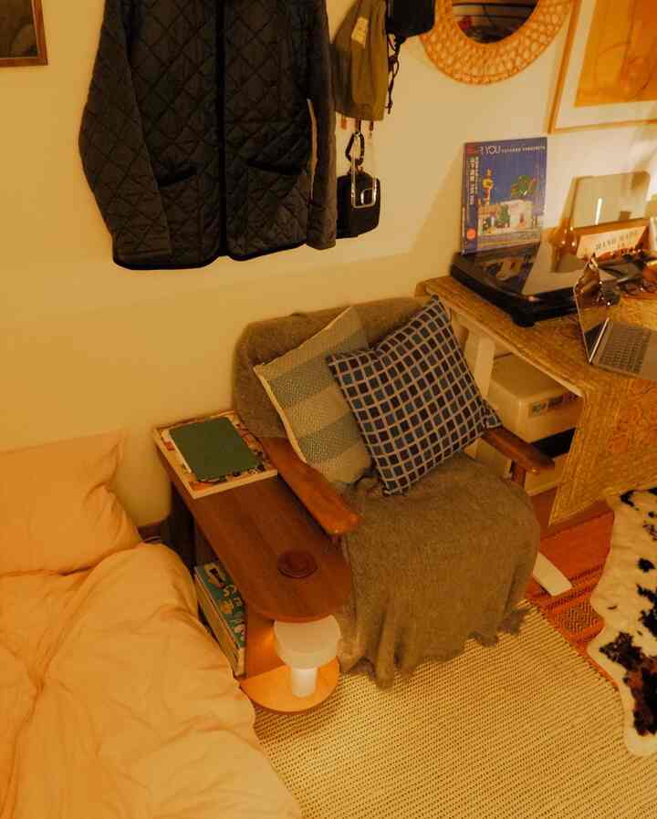 Beige and natural toned compact studio featuring bed, armchair, and wooden tables with a warm cozy atmosphere