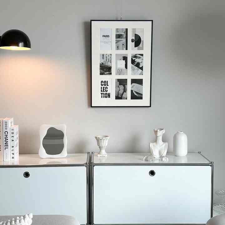 グレーの壁に並ぶ白いモジュール収納と複数の白いオブジェ、ブラックフレームのアートが配されたモダンなリビング空間