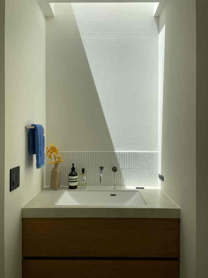 ナチュラルトーンの小さなバスルーム、木製キャビネットと白い洗面台、青いタオルが調和した雰囲気のあるインテリア