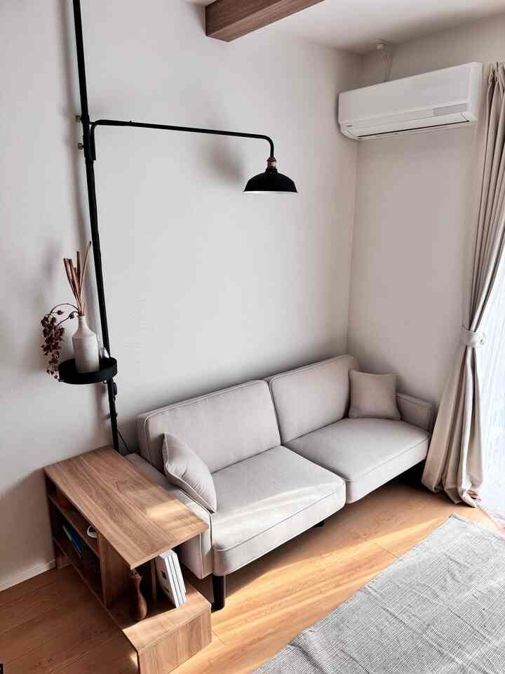 ナチュラルカラーと木目調が調和したリビング、コーナーソファとサイドテーブル、壁に取り付けられたフロアランプが温かみのある雰囲気を演出するインテリア