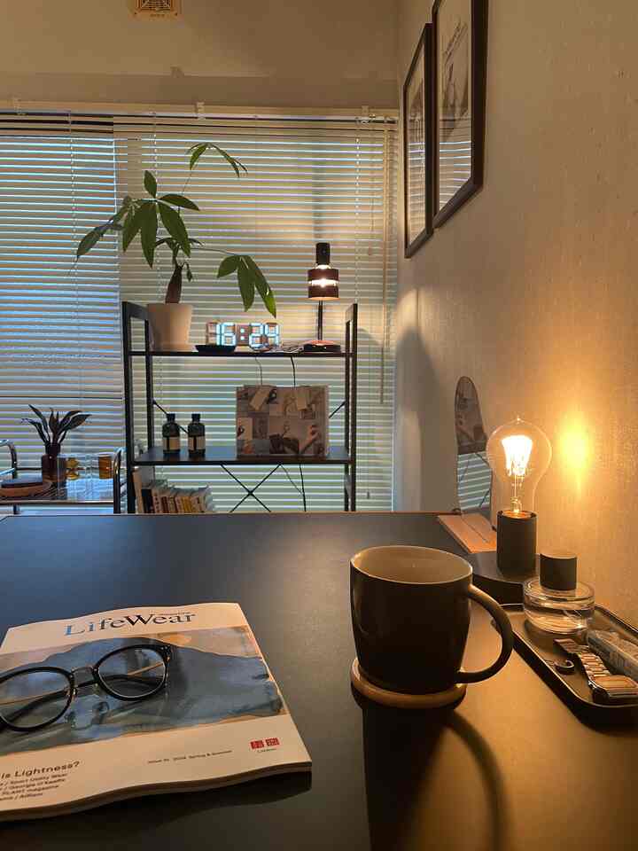 温かみのある照明と自然光に包まれたブラインド付きダイニングルーム、モダンなテーブルと植物が配置された落ち着いた空間