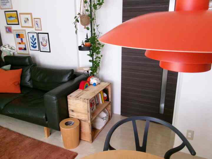 Natural-toned living room with green sofa, orange pendant light, hanging plants, and toy storage creating a cozy atmosphere