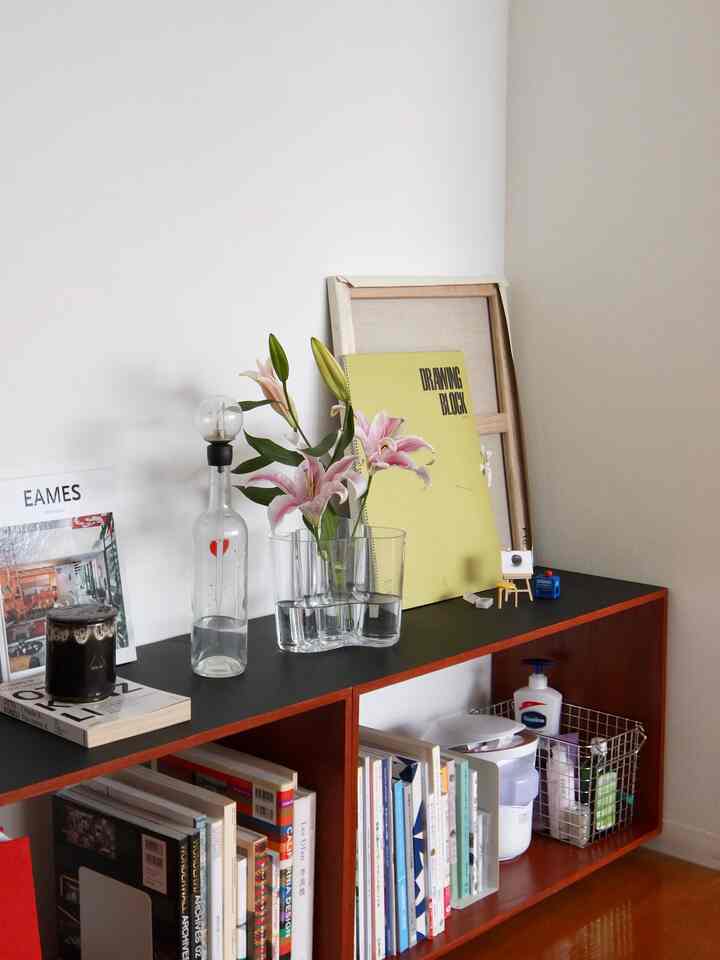 ホワイトの壁とブラウンの木製棚が配置されたナチュラルカラーの清潔感あるインテリア、花瓶と本が飾られている