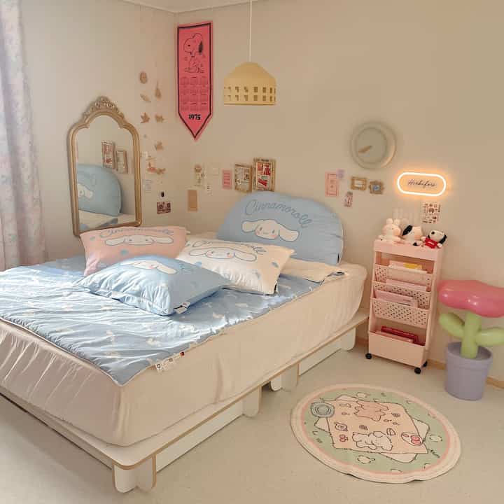 パステルトーンの寝室、シナモロールのキャラクター寝具とピンクの収納ワゴン、木製のペンダントライトが配置された雰囲気のあるインテリア