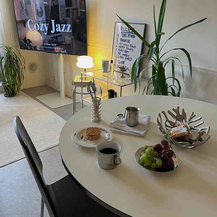 Simple 1LDK living room with white and black tones, featuring a round table topped with coffee and fruit