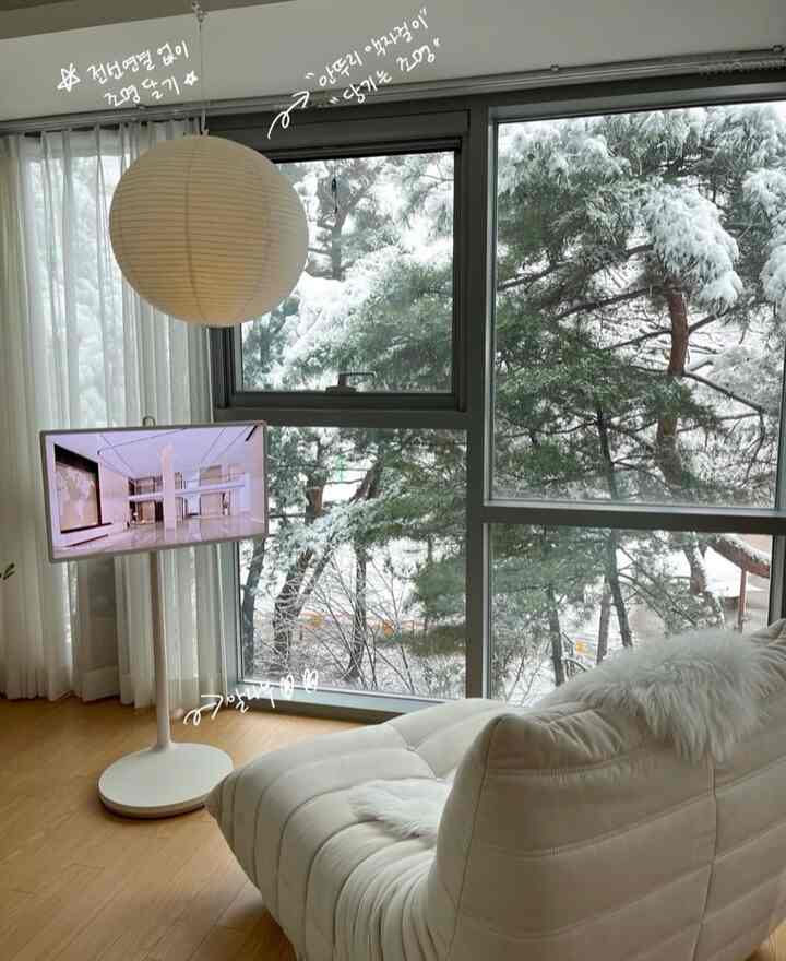 ホワイトとナチュラルウッドトーンが調和するリビング、クリーム色のソファとペーパーランプのシーリングライト、広い窓とカーテンが配置された雰囲気のある空間