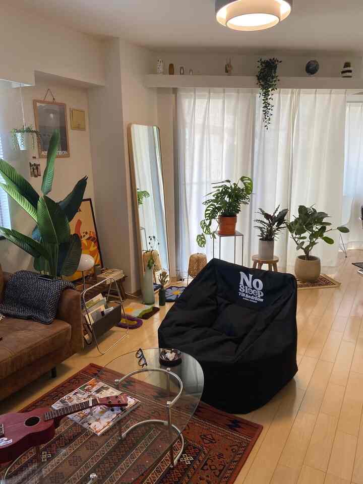 ナチュラルな色調のリビング、様々な植物とビーンバッグチェア、ガラステーブルとラグが調和した暖かみのある空間