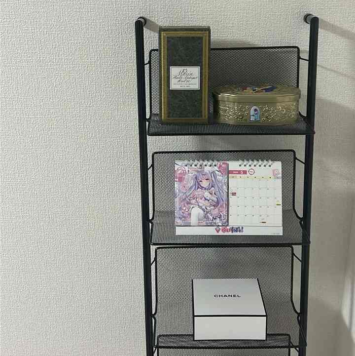 Beige wall with black mesh wall shelf in simple interior featuring various decorative items stored neatly
