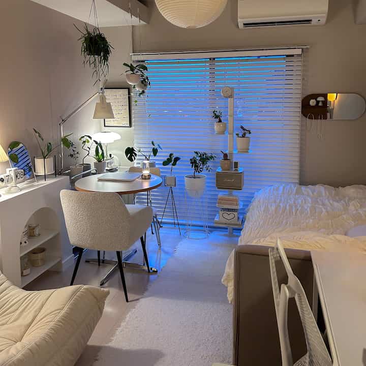 ベージュとナチュラルカラーの一人暮らしのリビング兼寝室、ダイニングテーブルとアームチェア、植物が配置された落ち着いたモダンな空間